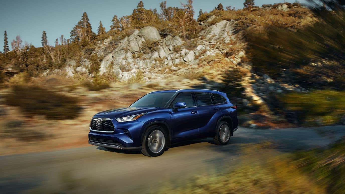 A blue Toyota Grand Highlander driving down the road near a rocky area