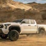 A silver Toyota Tacoma kicking up dirt as it drives off-road in a desert
