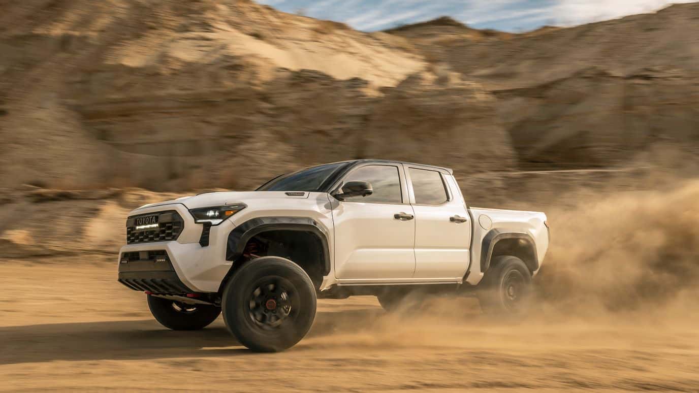 A silver Toyota Tacoma kicking up dirt as it drives off-road in a desert