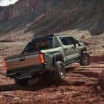 A rear view of a green Toyota Tacoma driving over a rocky environment.