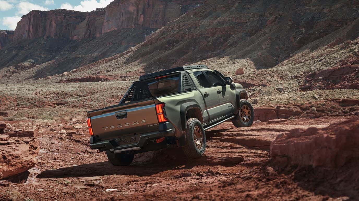 A rear view of a green Toyota Tacoma driving over a rocky environment.