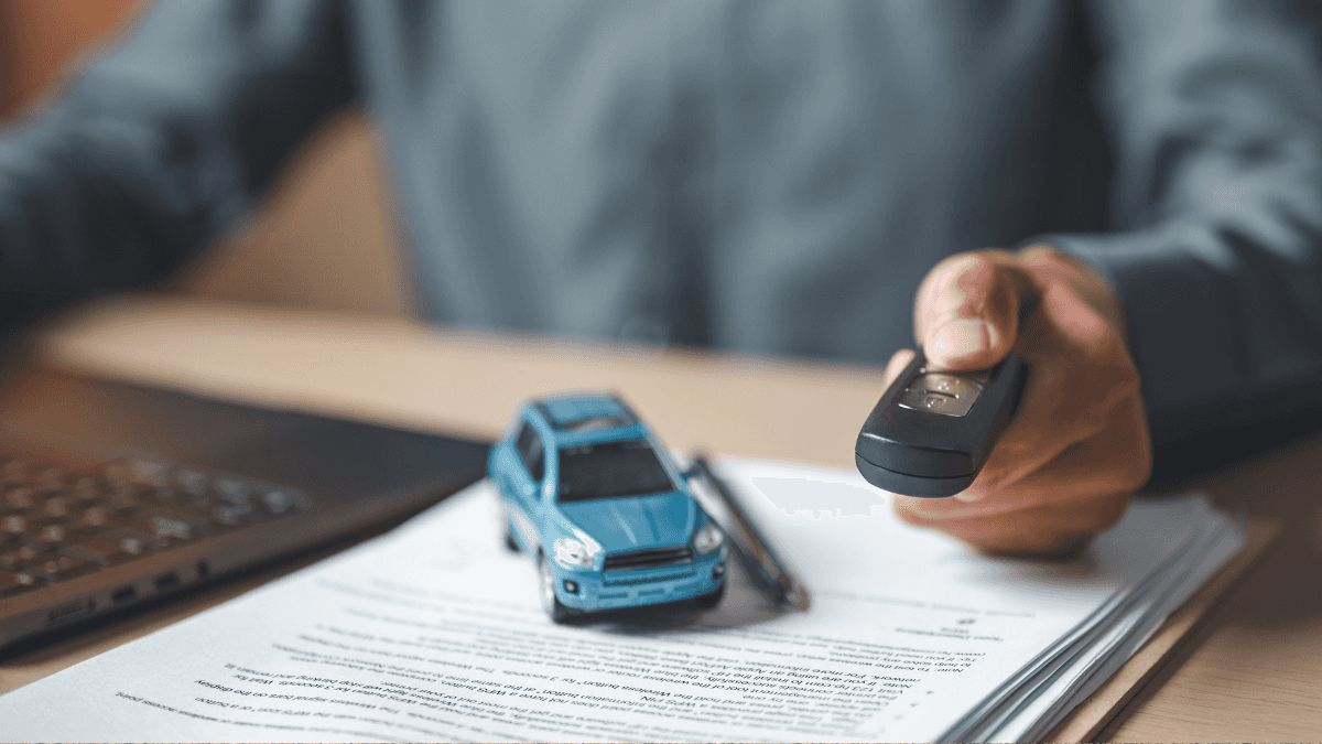 A man handing a key fob off with a light blue toy car on a stack of auto loan documents