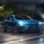 A light blue Toyota Camry driving through rain at night