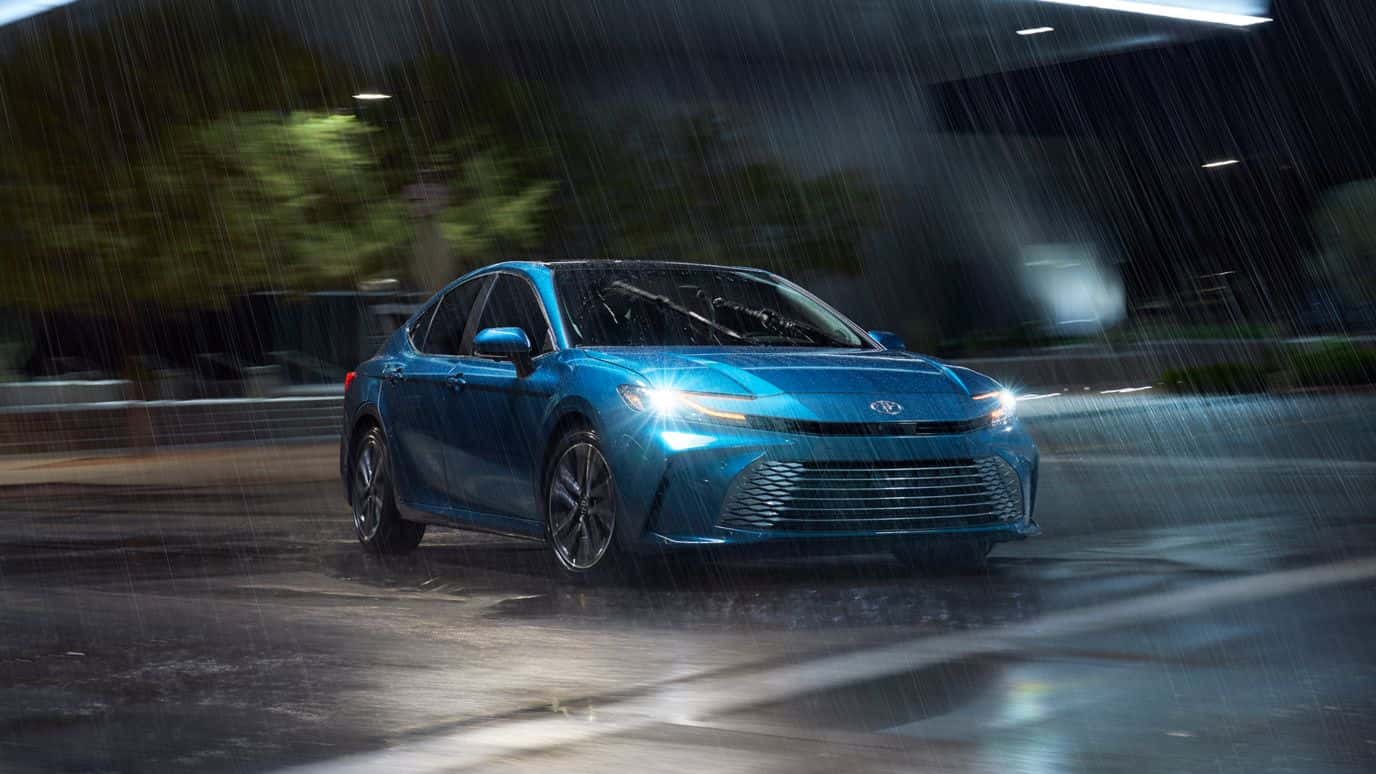 A light blue Toyota Camry driving through rain at night