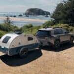 A gray Toyota RAV4 towing a small trailer on a dirt road on a cliff near a beach