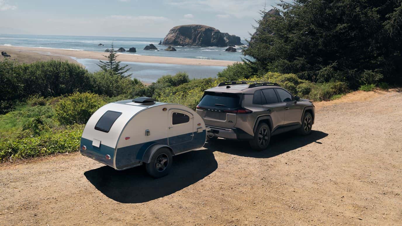 A gray Toyota RAV4 towing a small trailer on a dirt road on a cliff near a beach