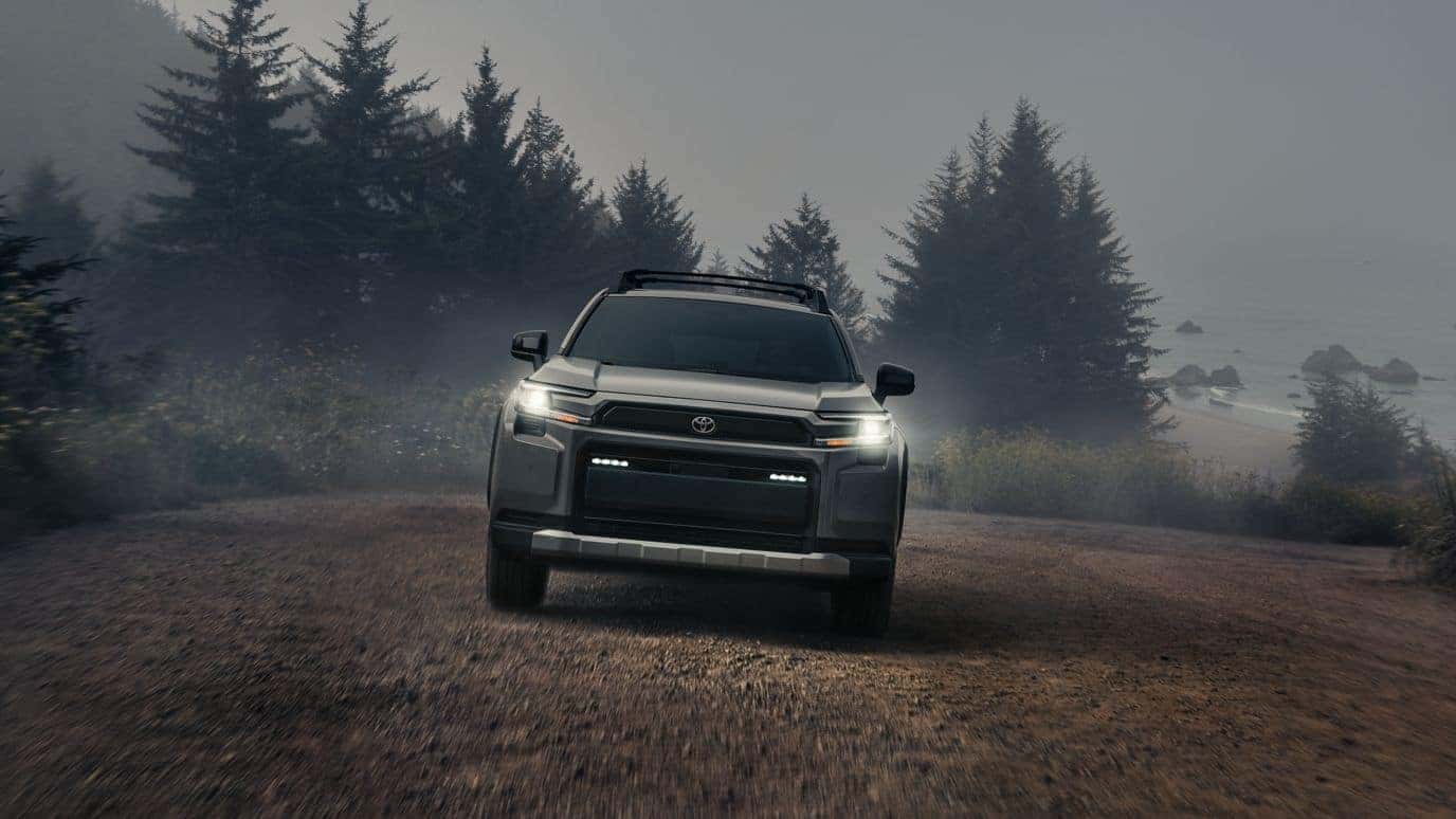 A front view of a green Toyota RAV4 driving off-road at night with its headlights on