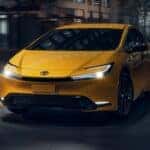 A front view of a yellow Toyota Prius driving down the road at night