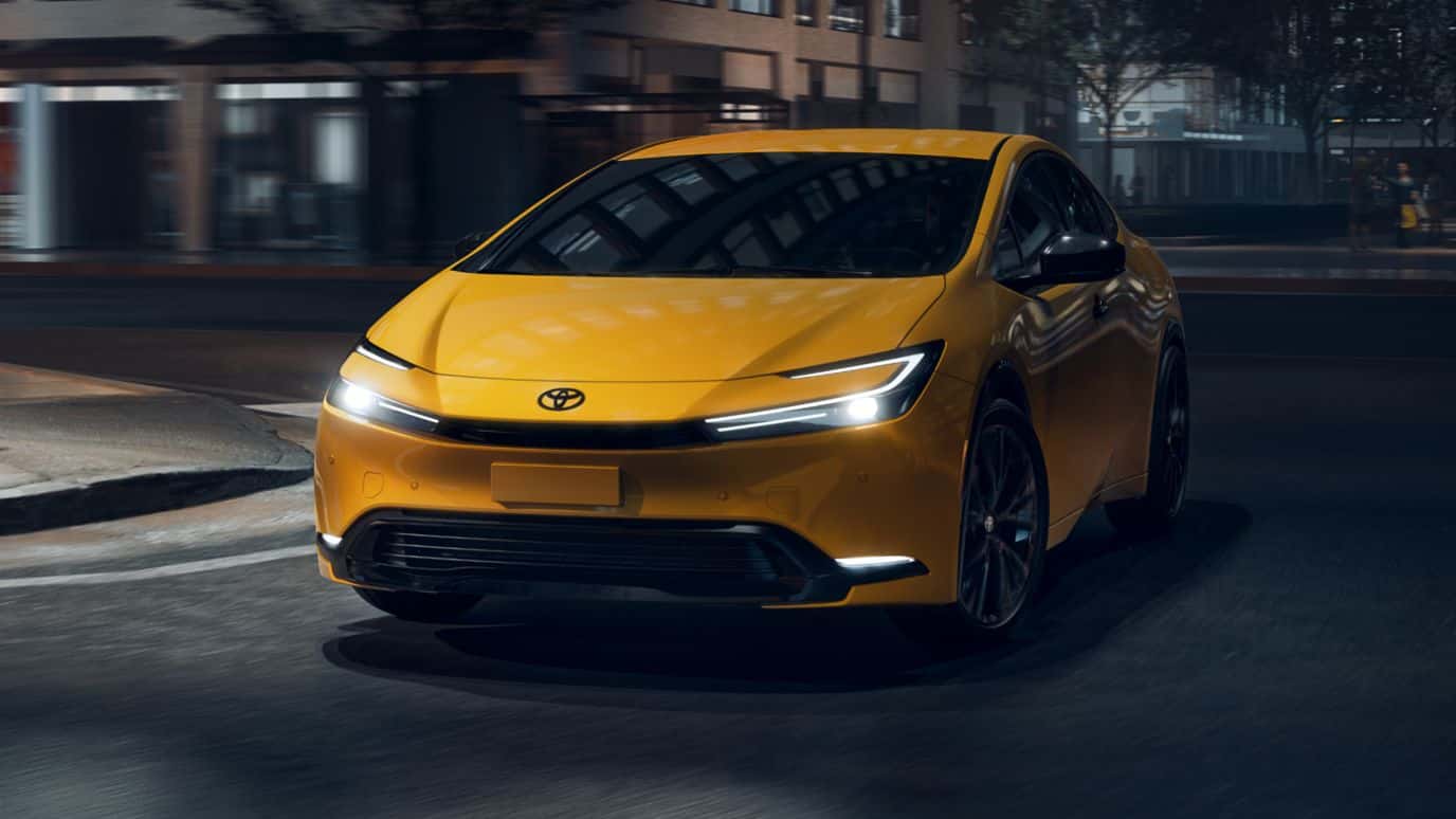A front view of a yellow Toyota Prius driving down the road at night