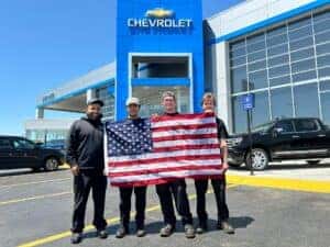 Four guys holding american flag in front of dealership