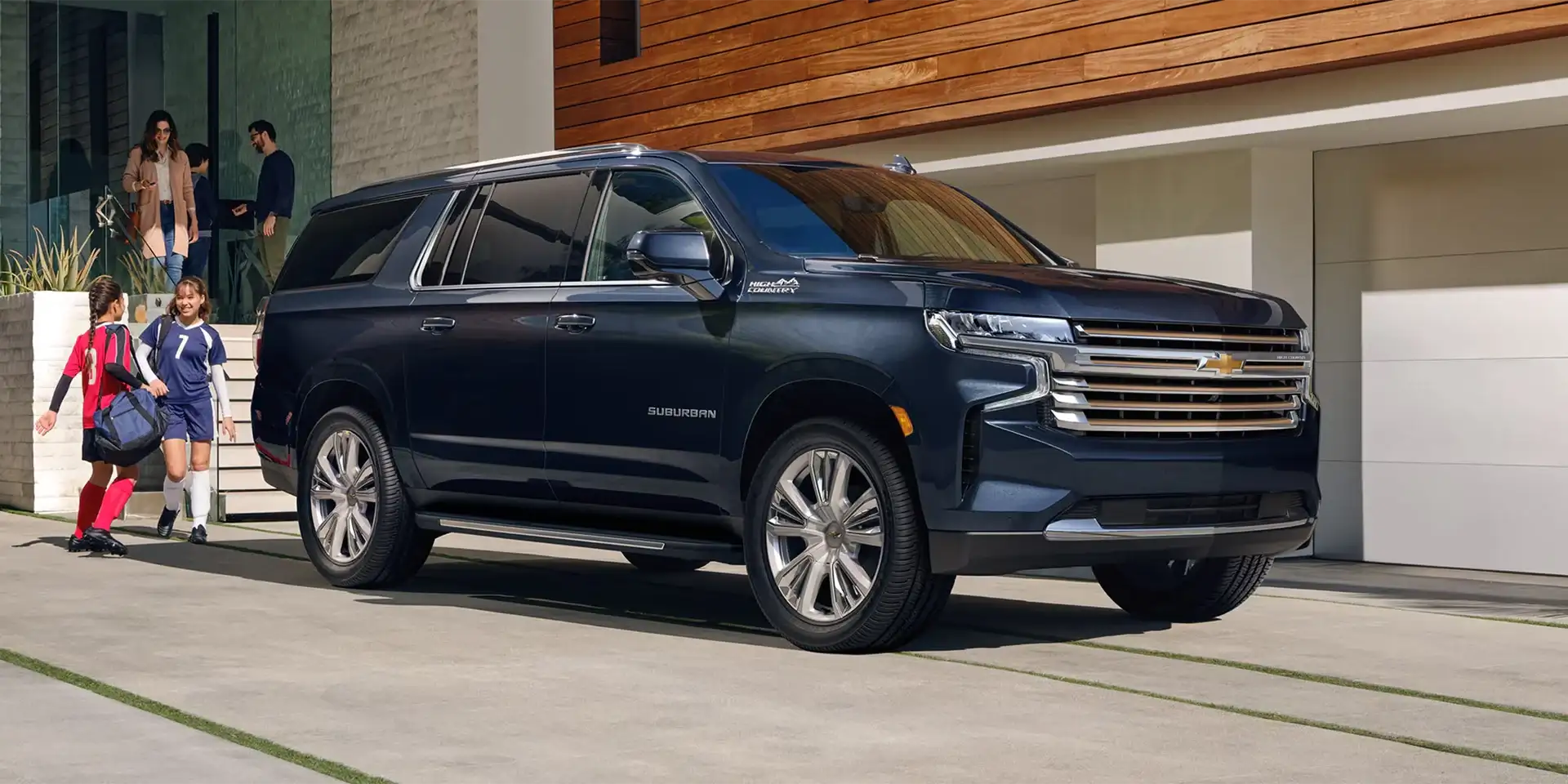 Family walking toward a dark blue Chevrolet SUV parked in a driveway