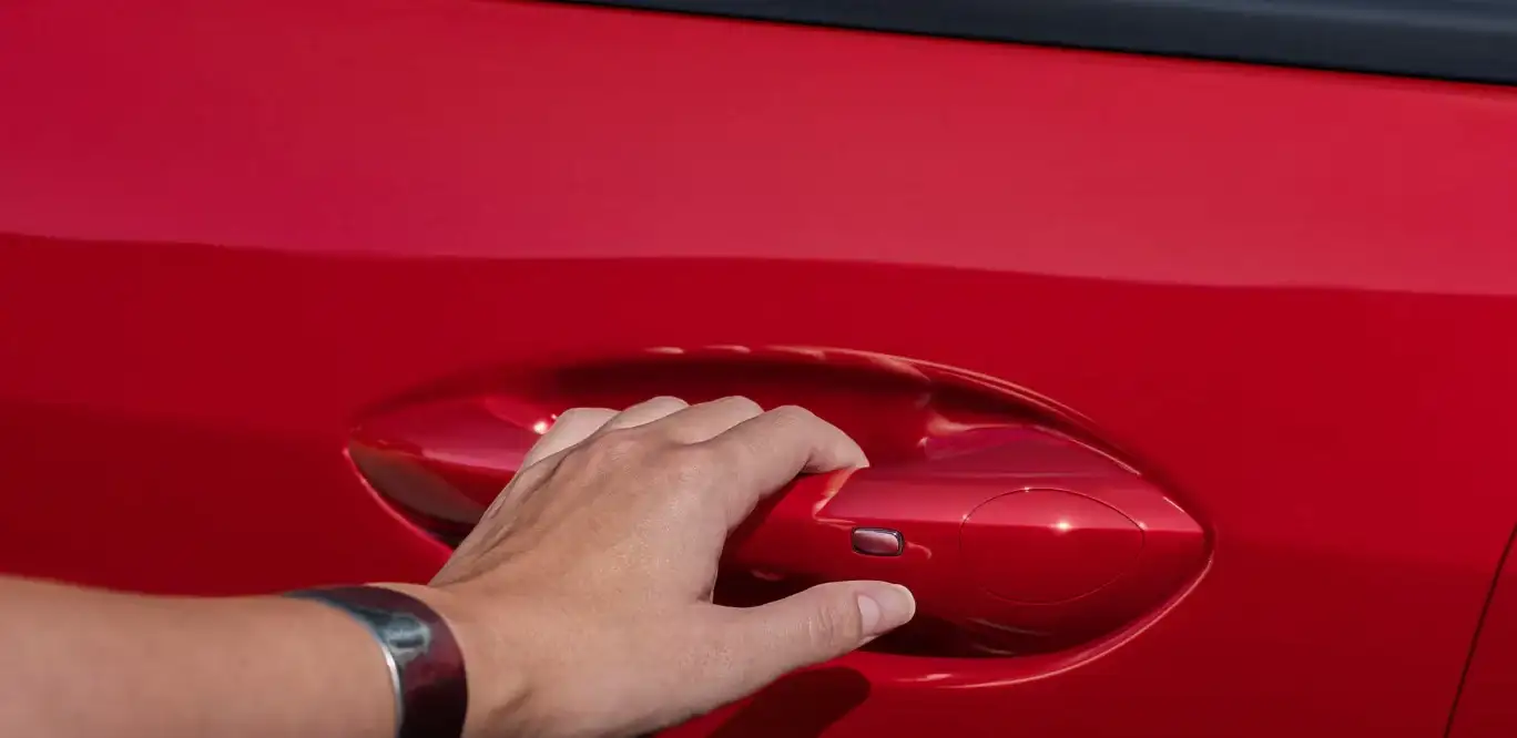 Hand reaching for the door handle of a red Chevrolet Trax