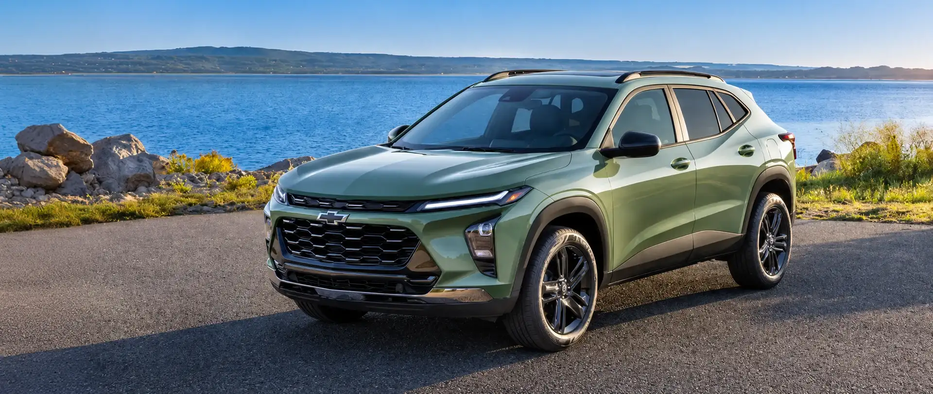 2026 Chevrolet Trax in sage green parked on a coastal road beside the water