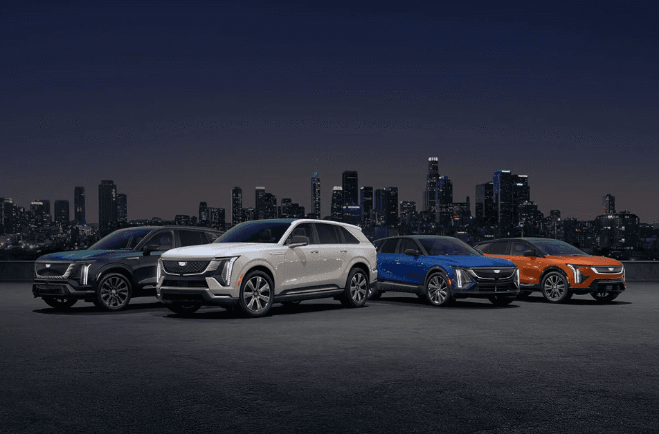 Cadillac EV Line-up featuring the VISTIQ, ESCALADE IQ, LYRIQ and OPTIQ - Four Cadillac EV SUVs in different colors parked with a city skyline behind them at dusk.  