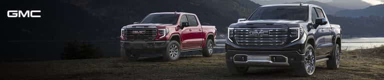 Front three-quarter view of GMC Sierra 1500 trucks showcasing chrome grilles parked in a mountain landscape.