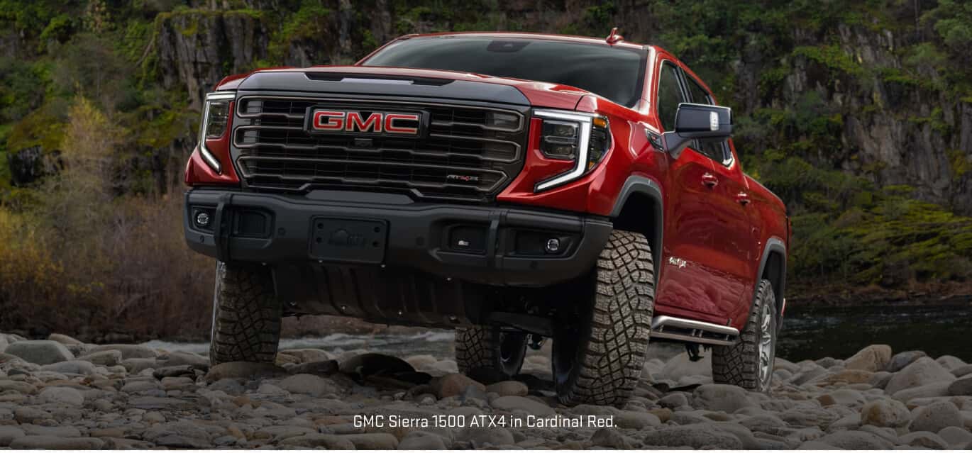 Low-angle front view of a GMC Sierra 1500 AT4X in Cardinal Red navigating a  rocky environment.