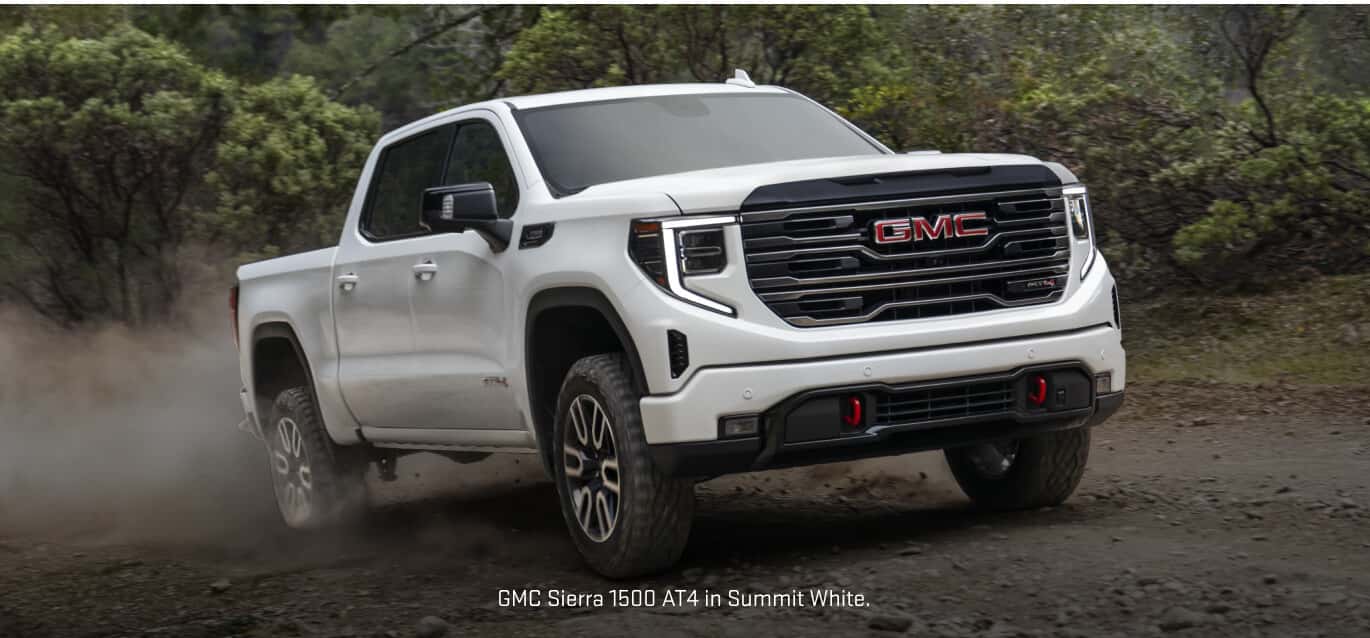 Front three-quarter view of a GMC Sierra 1500 AT4 in Summit White kicking up dust.
