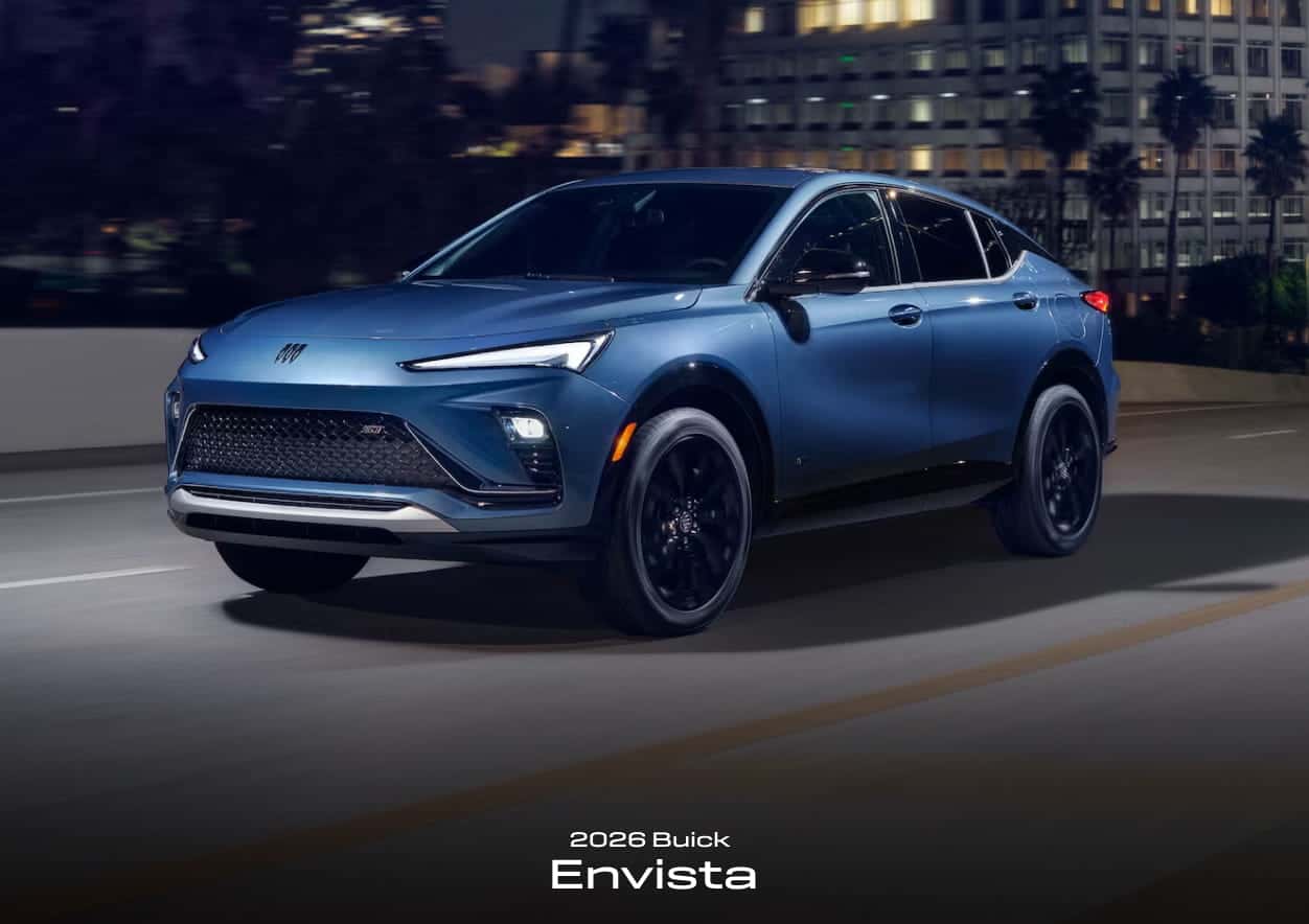 A sleek blue 2026 Buick Envista SUV drives along a city road at night.