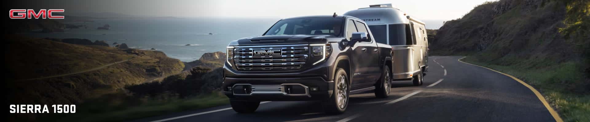 A 2026 GMC Sierra 1500 truck towing a silver trailer on a scenic coastal road.
