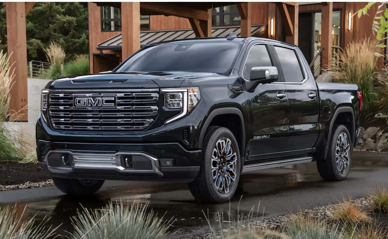 A sleek black 2026 GMC Sierra 1500 truck is parked in front of a modern wooden house.