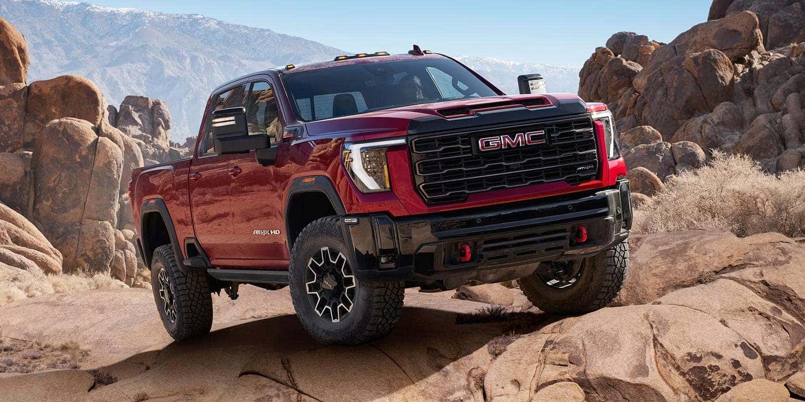An off-road capable, deep red GMC Sierra HD AT4X truck is pictured navigating a rugged, rocky desert landscape near Chaparral Buick GMC