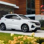 Passenger front 3/4 view of 2023 Buick Encore GX in White Frost Tricoat parked in the driveway of a home