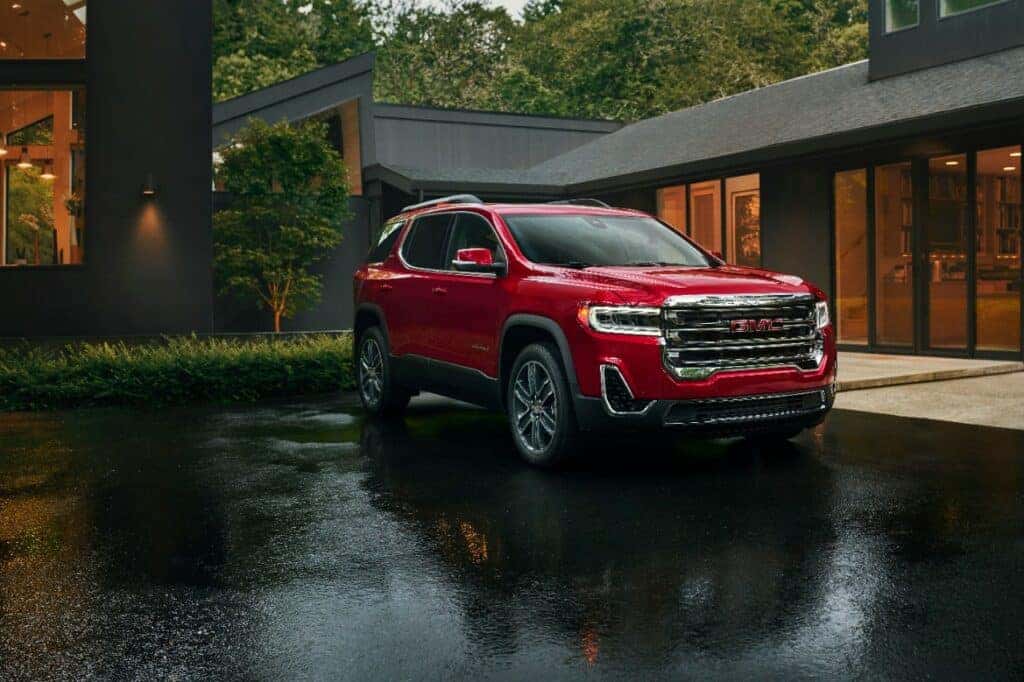 Passenger front 3/4 view of 2023 GMC Acadia SLT in Volcanic Red Tintcoat with house in background