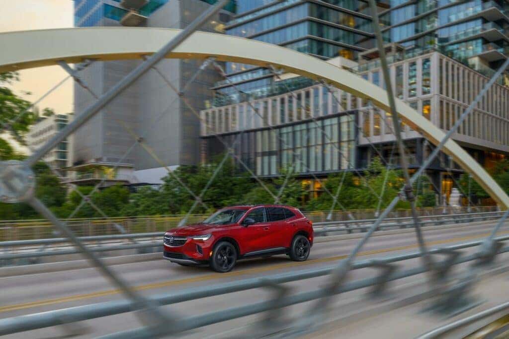Driver front 3/4 view of 2023 Buick Enclave in Cinnabar Metallic driving on bridge.