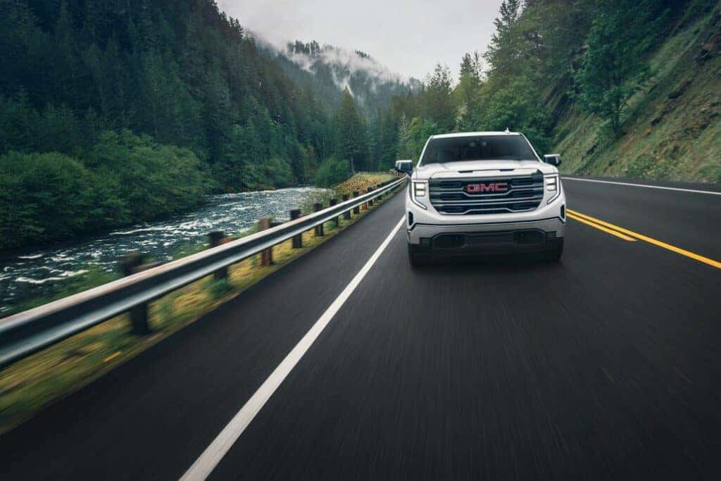 2024 GMC Sierra 1500 SLT Crew Cab Short Box 4WD in White Frost Tricoat. Direct front image in motion, driving on bridge next to river.