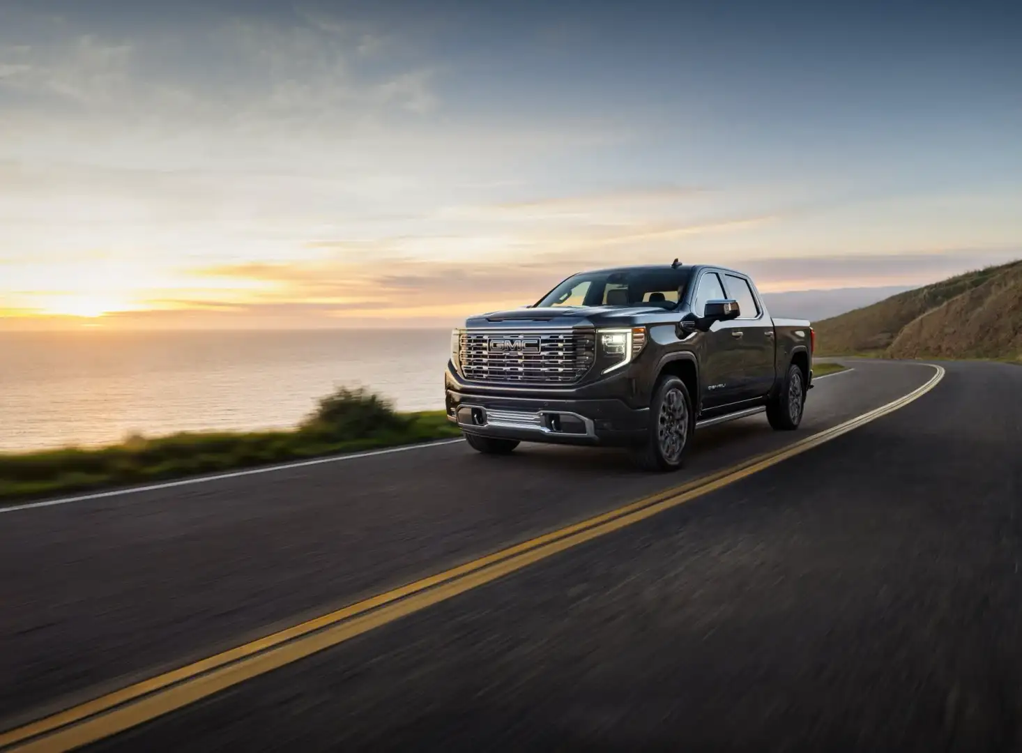 2026 GMC Sierra Denali Ultimate driving on a road at sunset 