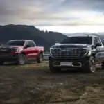 2026 GMC Sierra Trucks parked off road in front of a lake and mountains
