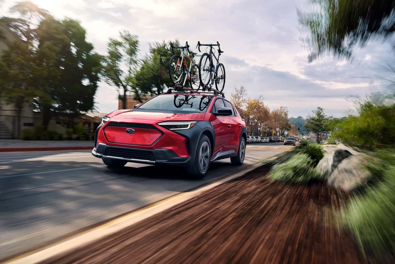 2025 red Subaru Solterra driving on the road with bikes on roof rack