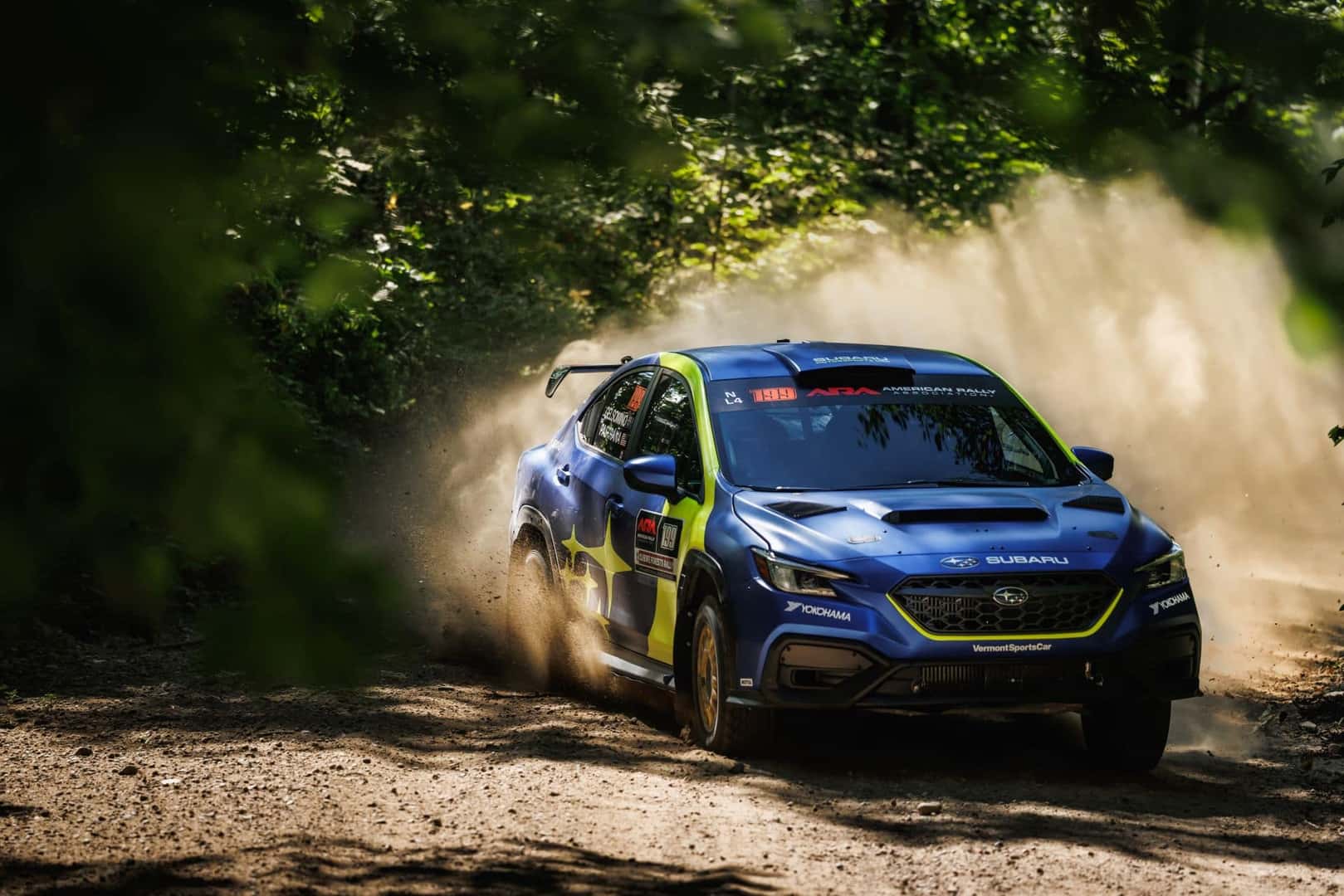 The Subaru Motorsport's Team's WRX Racing Through The Thick Forest, Leaving A Dust Trail Behind