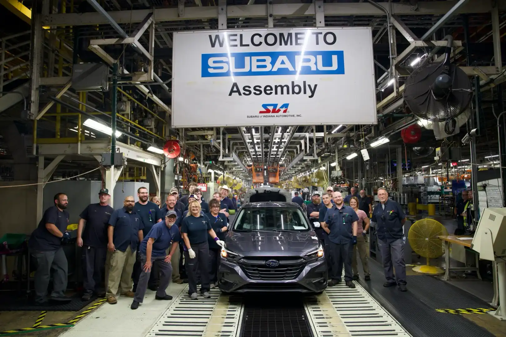 Subaru of Indiana Automotive Assembly line workers around a Grey Subaru Legacy