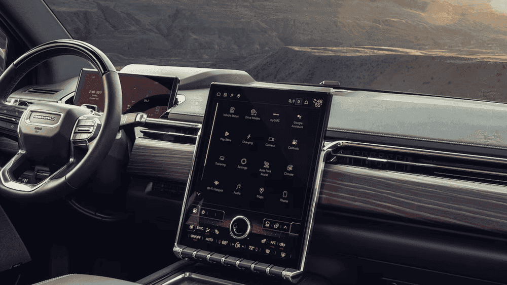 2026 GMC Sierra EV Denali interior dashboard near Ruth NC with Denali-branded steering wheel, large vertical touchscreen showing Google Assistant, Drive Modes, and Charging, with desert mountain backdrop