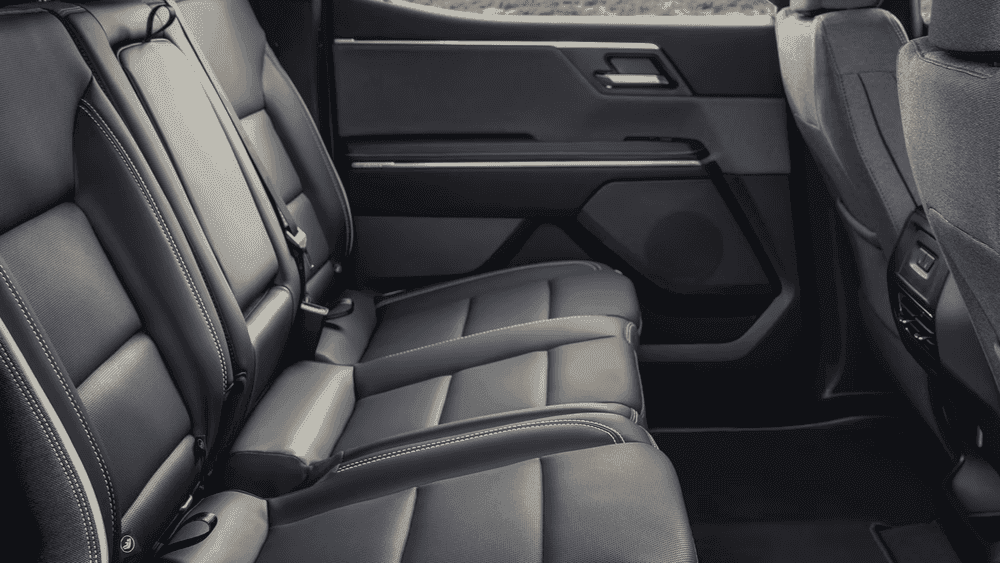 2026 GMC Sierra EV rear passenger cabin near Ruth NC with black leather bench seating, white contrast stitching, fold-flat center seat, and rear door panel storage visible