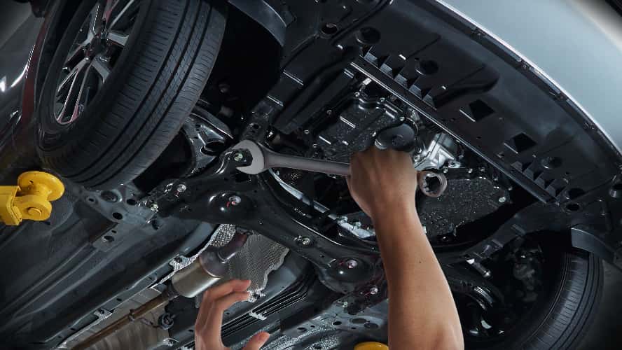 A mechanic working on a vehicle's undercarriage.
