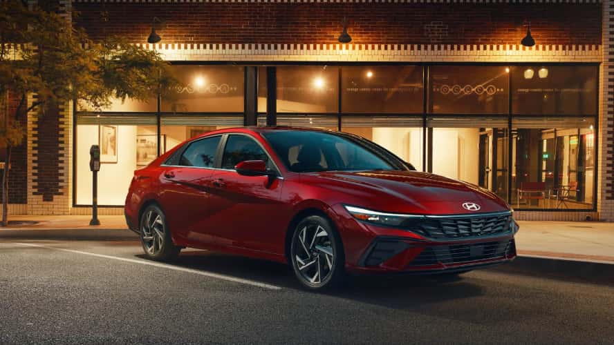 A red Hyundai Elantra parked in a space in front of a building at night.