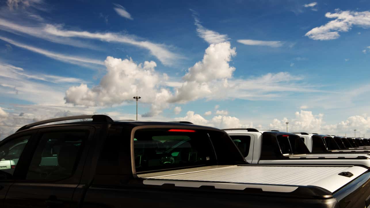 A row of pickup trucks in a dealership lot with their truck beds covered.