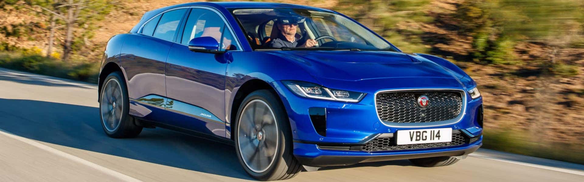 2024 blue jaguar i pace driving down road during sunset