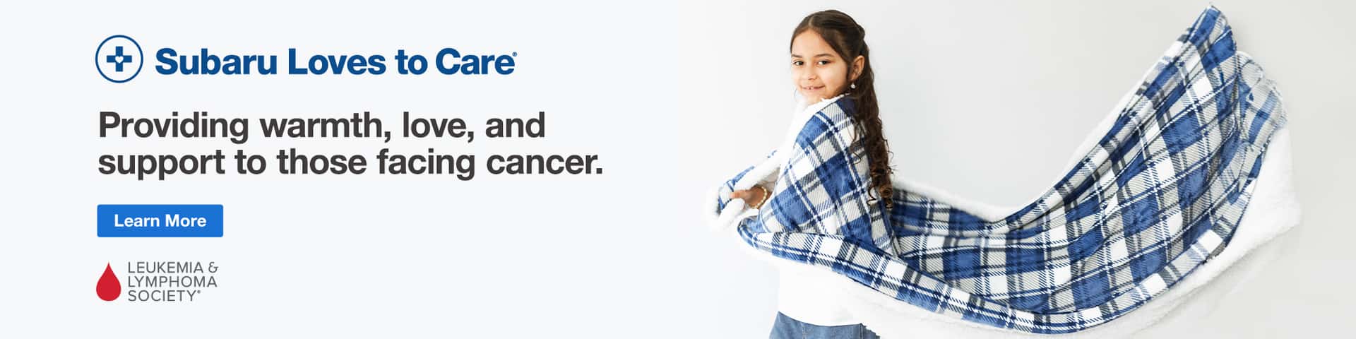 Subaru Loves to Care. Young girl smiling wrapped in blue flannel blanket