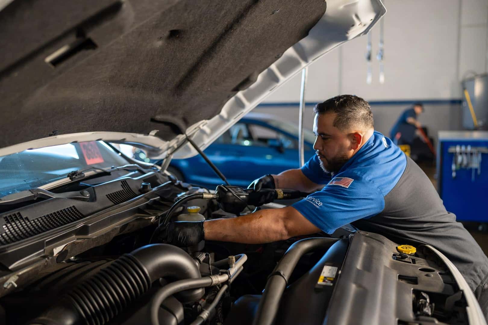 A technician at Knight Claremont Chrysler Dodge Jeep Ram working in the engine bay of a white Ram pickup under an open hood