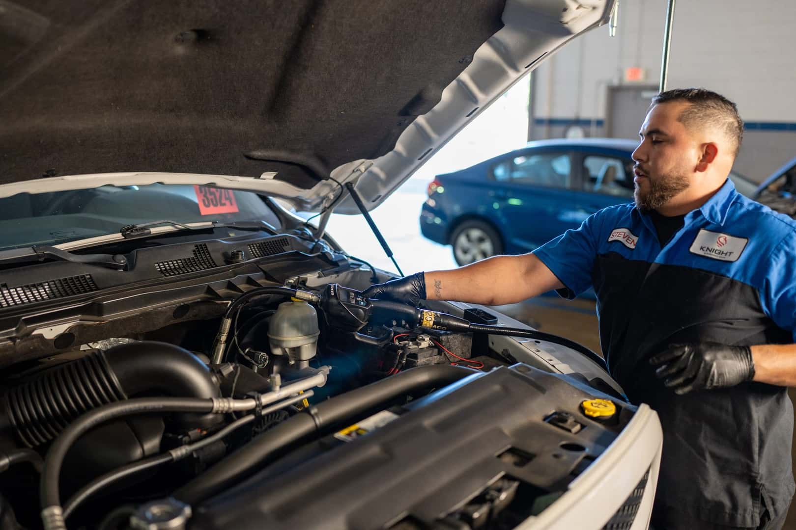 A technician at Knight Claremont Chrysler Dodge Jeep Ram checking under the hood of a white Ram pickup in the service shop