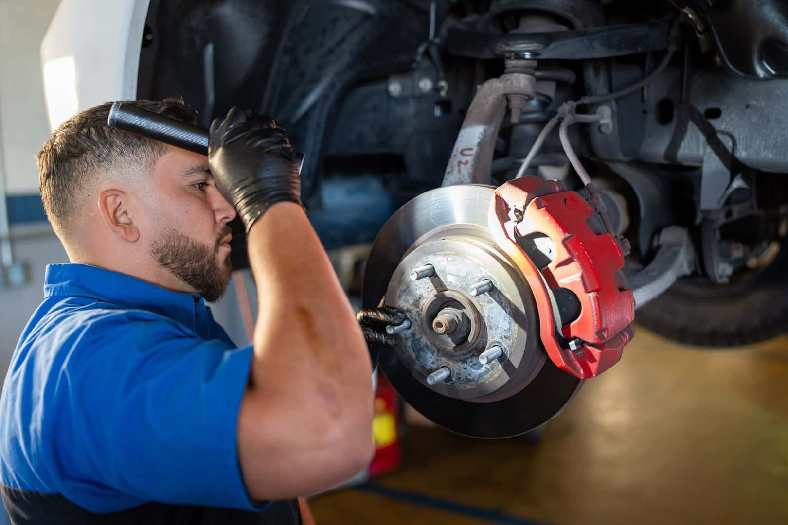 A technician at Knight Claremont Chrysler Dodge Jeep Ram inspecting a brake rotor and red caliper on a pickup with the wheel removed
