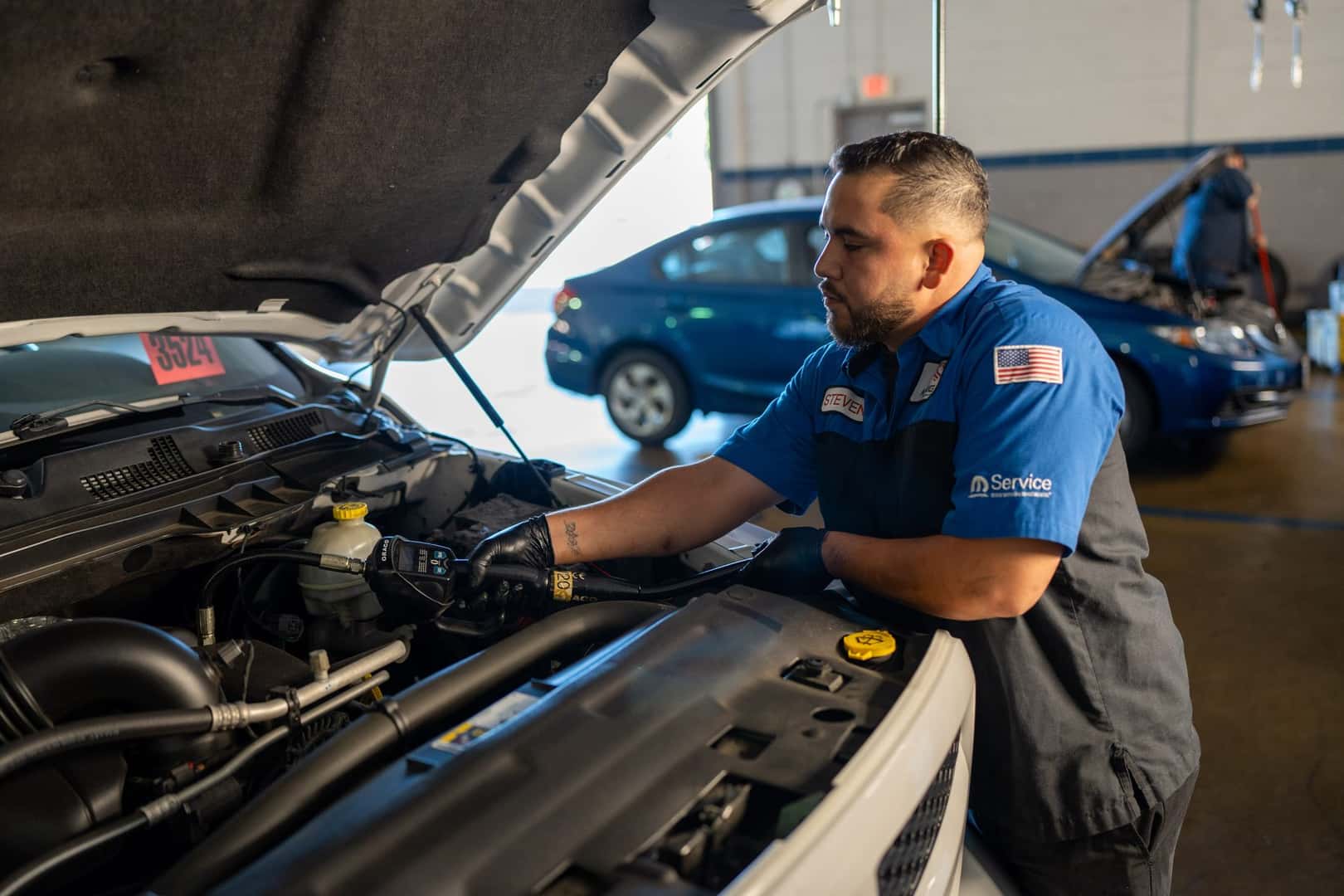 A technician at Knight Claremont Chrysler Dodge Jeep Ram working in the engine bay of a white Ram pickup under an open hood