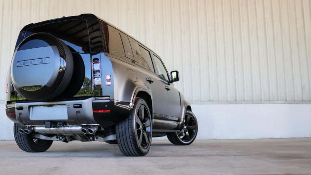 Rear view of the 2025 Land Rover Defender highlighting its signature side-hinged tailgate, full-size spare tire, and modern LED taillights.