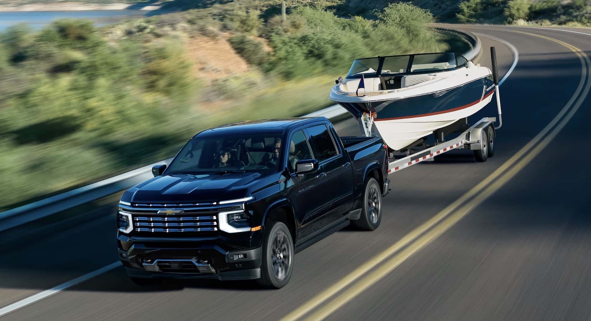 Black 2027 Chevrolet Silverado 1500 exterior towing a boat and trailer on a highway