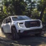 White 2024 GMC Acadia AT4 driving on a trail