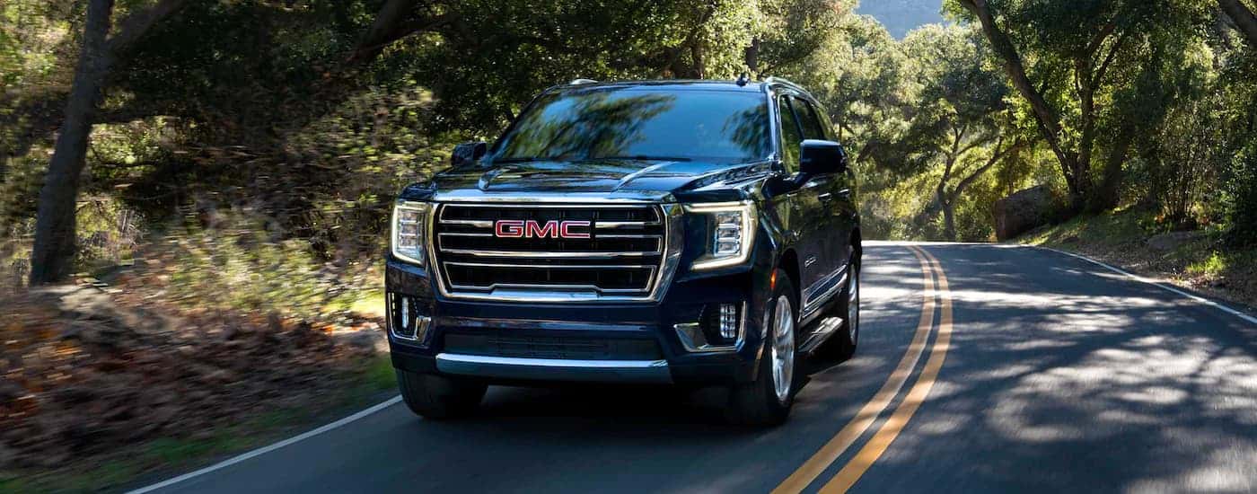 Black 2023 GMC Yukon driving on a heavily forested road