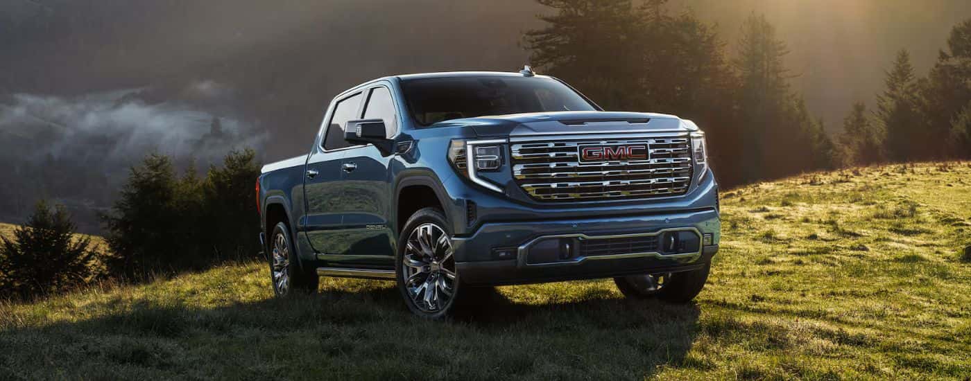 Blue 2026 GMC Sierra 1500 Denali parked in a green valley at sunrise
